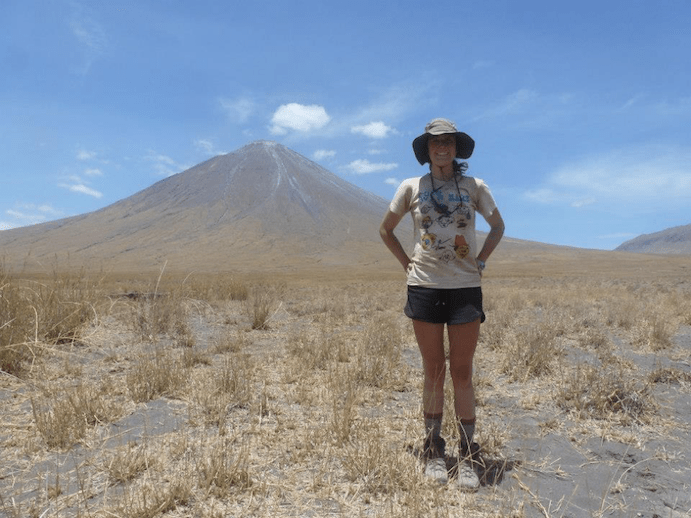 Brenna stands confidently with her hands on her hips. In the background is the Great Rift Valley and Ol Doinyo Lengai.