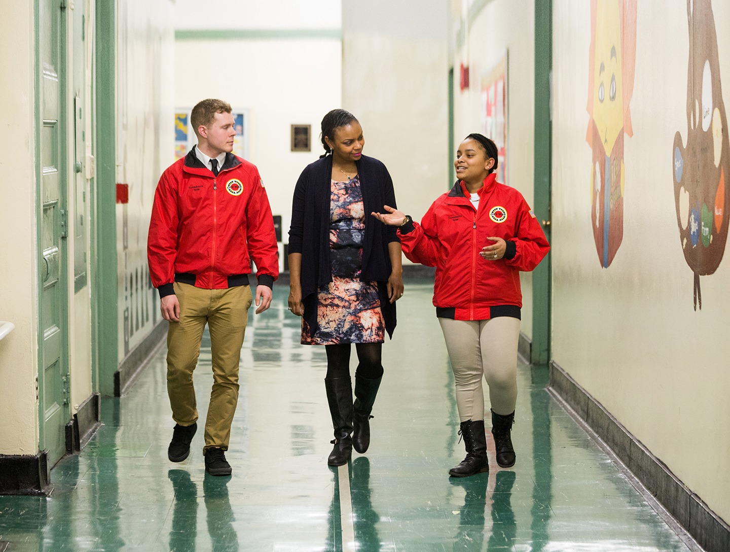Two AmeriCorps members walking and talking with a City Year team supporter in a school hallway