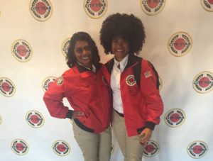 Two AmeriCorps Members pose in front of a backdrop decorated with City Year logos