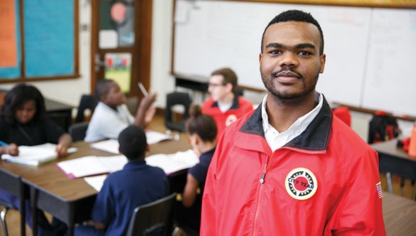 AmeriCorps member in classrrom with students and corps member working behind them at a table