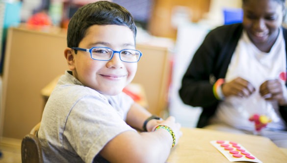 smiling elementary student doing a project at a table with an AmeriCorps member