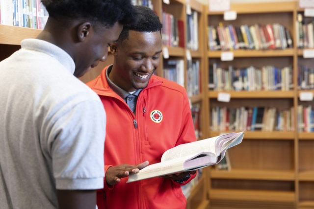 an AmeriCorps member is holding a book and reading with a student in the library