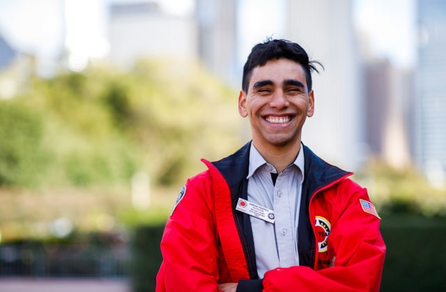 An AmeriCorps member stands in a park with the city skyline in the background.