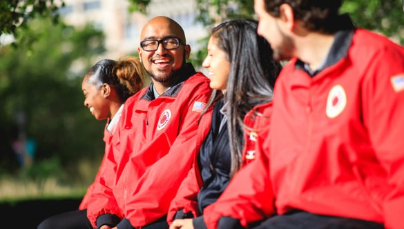 A group of AmeriCorps members sit outside their school and chat.