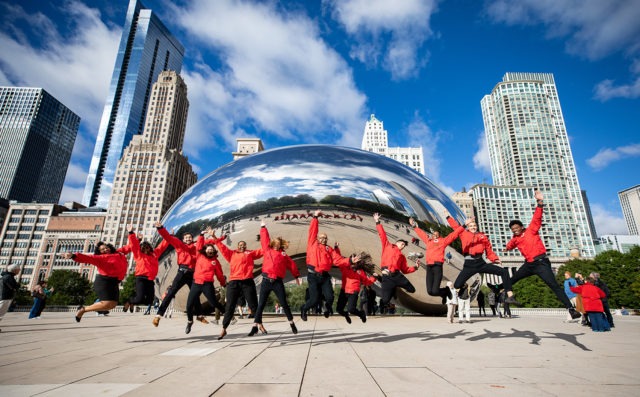 A group of AmeriCorps members jump and cheer in front of the city skyline.