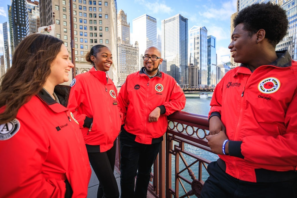 A group of AmeriCorps members are gathered on a walking bridge in the city.