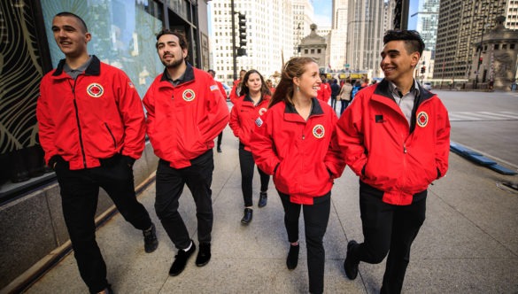 A group of AmeriCorps members walk along the city sidewalk.