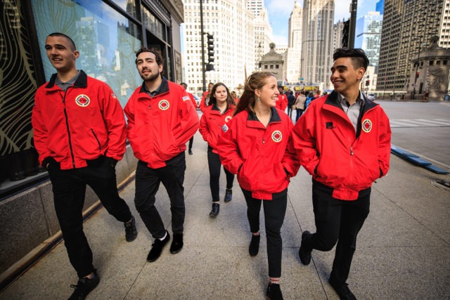 A group of AmeriCorps members walk along the city sidewalk.