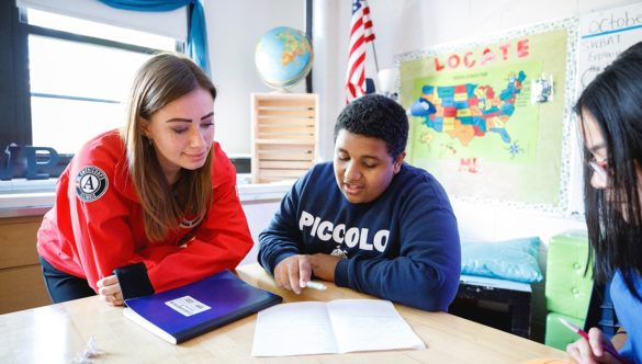 student is talking through a work assignment with an AmeriCorps member in the classroom