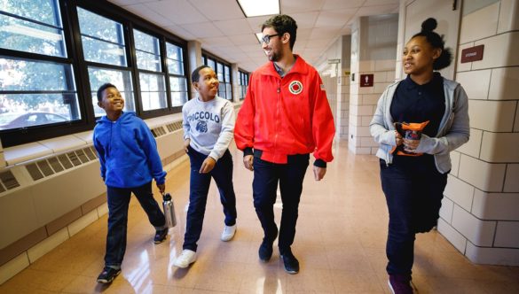 AmeriCorps member walks with three students in the hallway