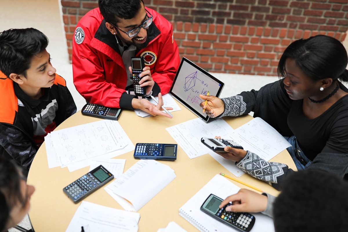 Four students with calculator, and papers with a City Year Corps Member who is showing a geometry problem