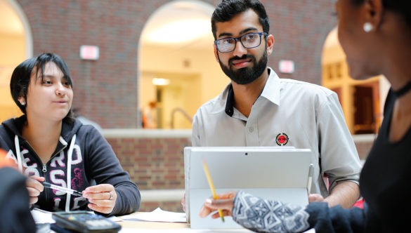 A City Year corps member with a tablet listening to two students around a table