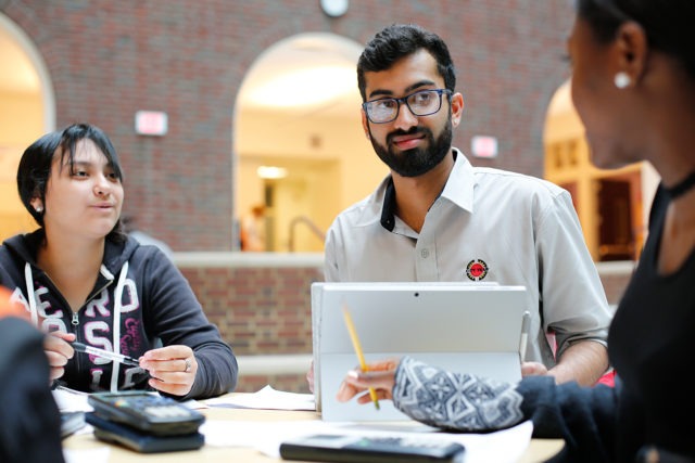 A City Year corps member with a tablet listening to two students around a table