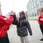 An elementary school student wearing glasses high fives a City Year AmeriCorps member outside their school