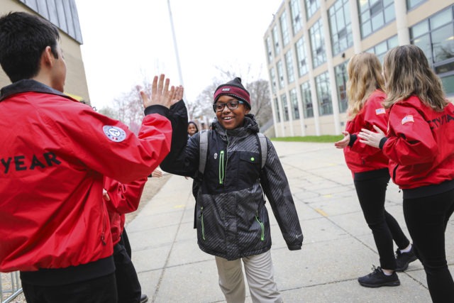 An elementary school student wearing glasses high fives a City Year AmeriCorps member outside their school