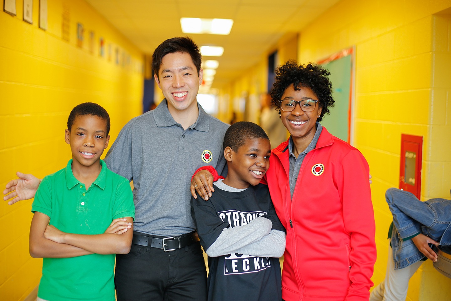 Two city year americorps members posing with two young students in a school hallway.