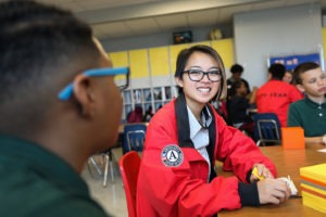 City year americorps member sitting at a table with a student with students and corps members in the background