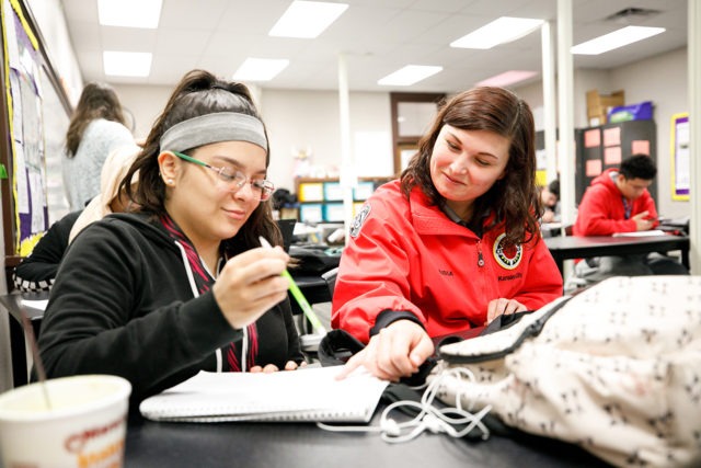 AmeriCorps member is pointing out something on high school student's page as they do work in the classroom