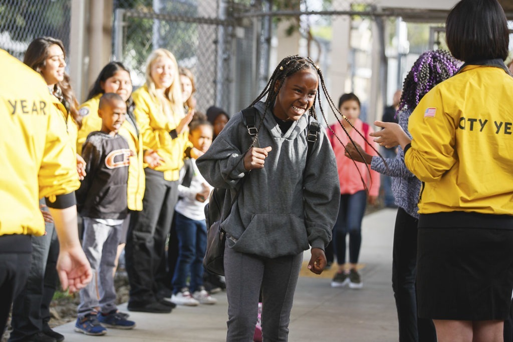 AmeriCorps members cheer on student outside of a school