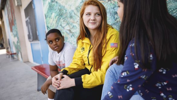 AmeriCorps member talks with student on bench while another listens