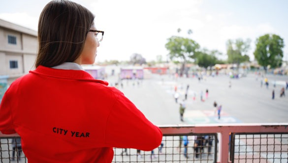 A city year americorps member standing on story above and looking down at a school courtyard full of students