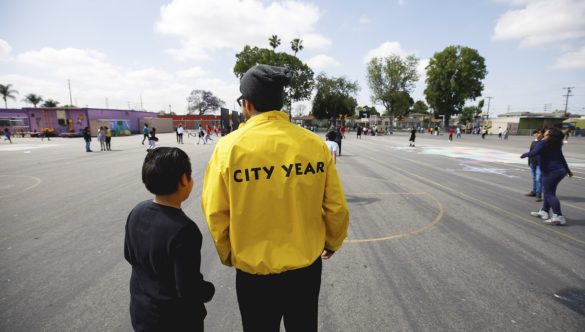 AmeriCorps member talking with student on playground while other students are playing