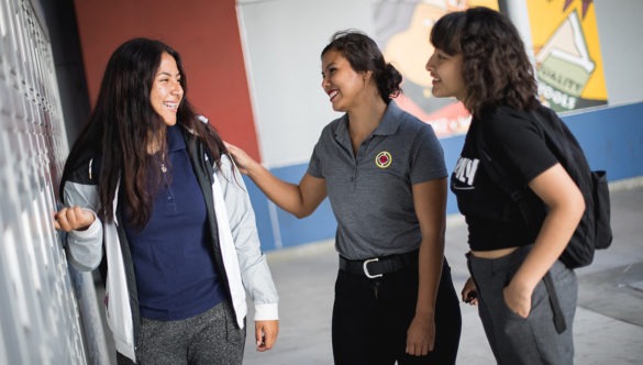 city year americorps member talking with a high school student as they stand in front of lockers in a school hallway
