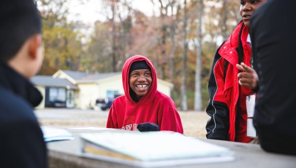 students are doing work at a table outside, smiling and working with their AmeriCorps members