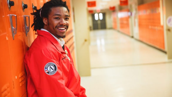 An AmeriCorps member leans again lockers in a school hallway.