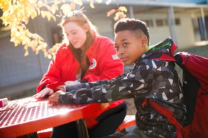 City year americorps member and a student with a backpack sitting at a table in a school courtyard in the sunshine