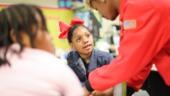 a student looks up at an AmeriCorps member as they help them at their desk