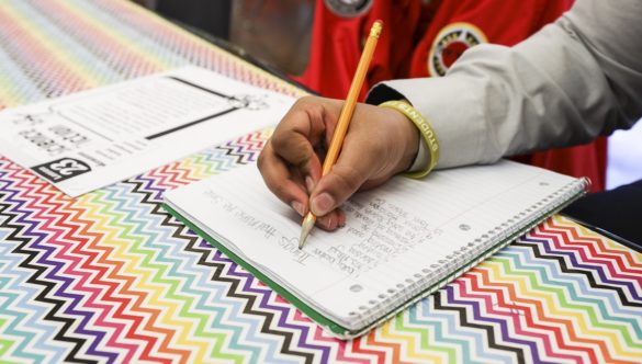 A student writes down notes with a pencil in a notebook.