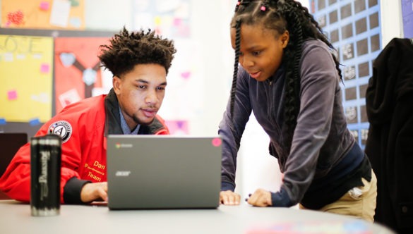 city year americorps member sitting with a student standing next to him as they both look at a laptop screen