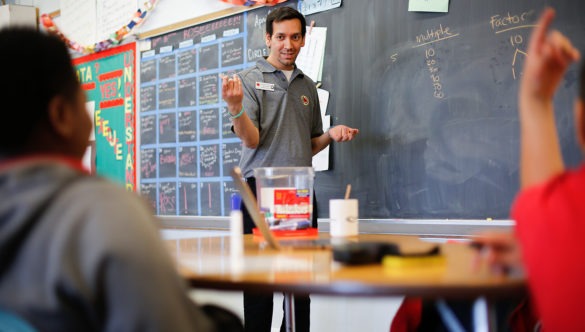 city year americorps member standing in front of a chalkboard showing multiples as students watch