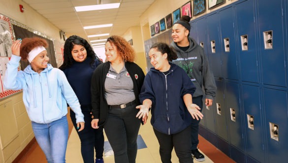 a city year americorps member walking with students in a hallway next to lockers