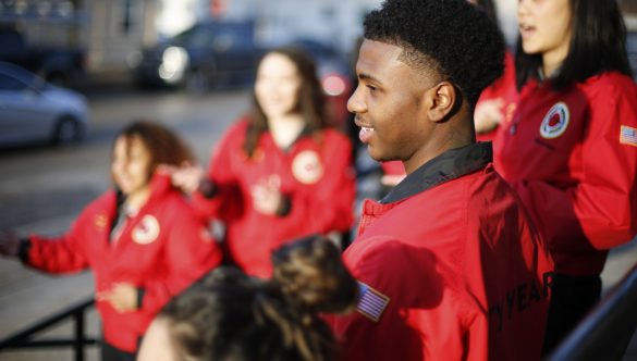 A profile of a City Year AmeriCorps member standing on the steps outside of a school