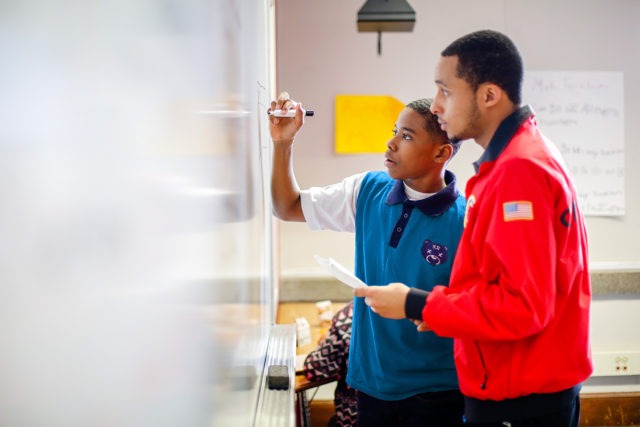 city year americorps member with a student who is writing on a whiteboard with a sharpie