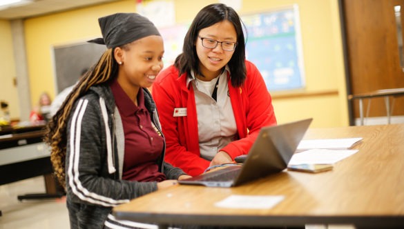 High school student working on a computer with an AmeriCorps member supporting