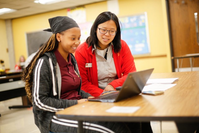 High school student working on a computer with an AmeriCorps member supporting
