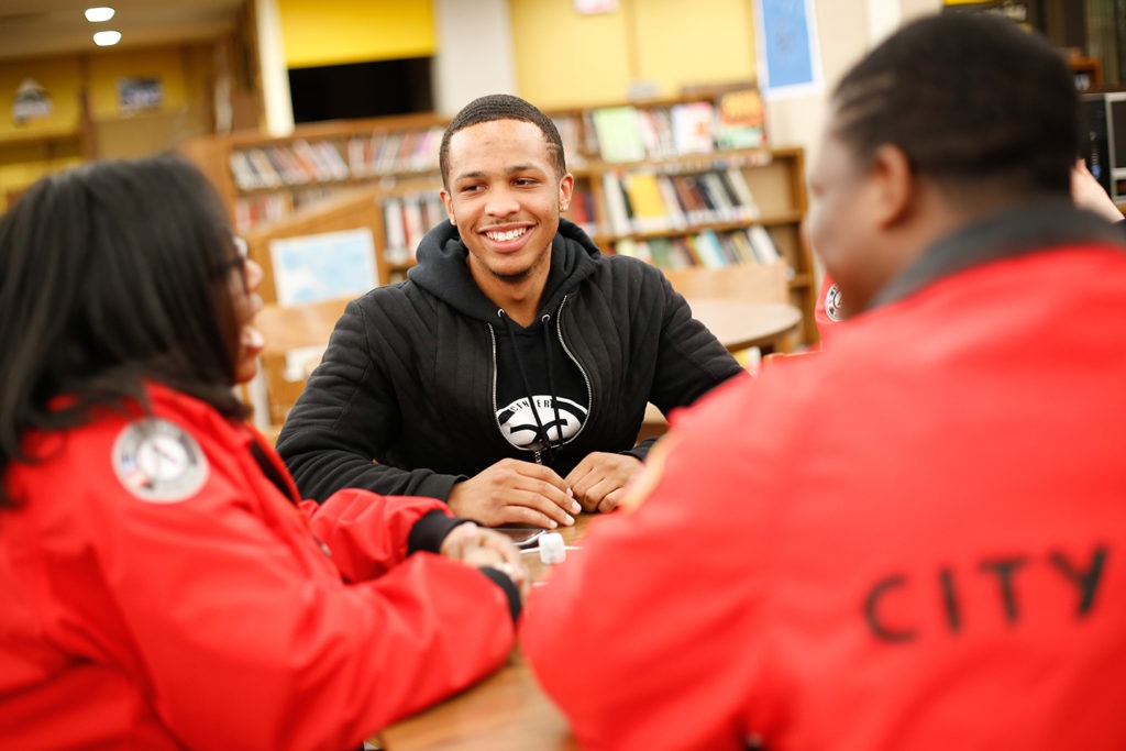 two AmeriCorps members talking with a high school student at a table in the library