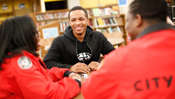 two AmeriCorps members talking with a high school student at a table in the library