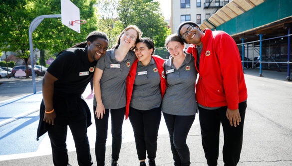 A group of AmeriCorps members are huddled together on the basketball court at a park.