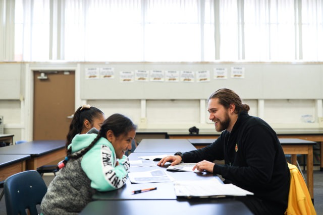 two students are joyfully doing their work, while supported by an AmeriCorps member in the library