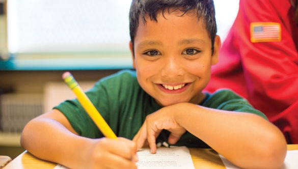 smiling elementary student doing worksheet at a desk