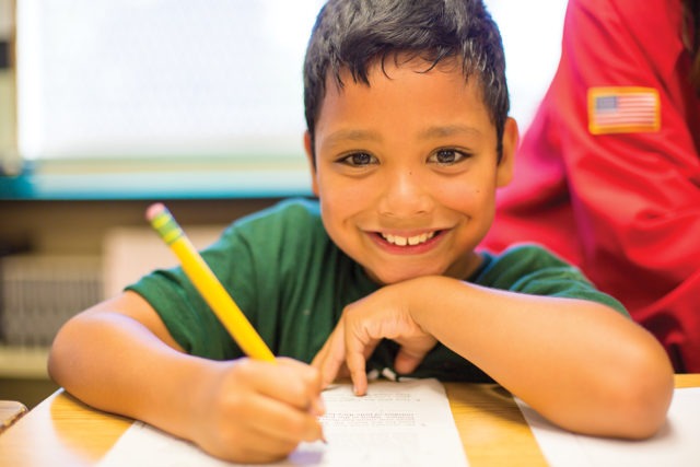 smiling elementary student doing worksheet at a desk