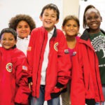 Group of elementary students smile while wearing their AmeriCorps members' jackets