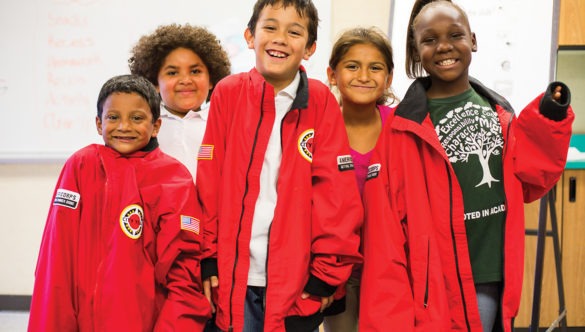 Group of elementary students smile while wearing their AmeriCorps members' jackets