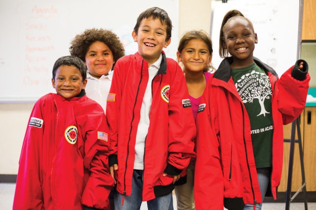 Group of elementary students smile while wearing their AmeriCorps members' jackets