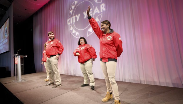 An AmeriCorps member raises her hand on stage at a City Year event