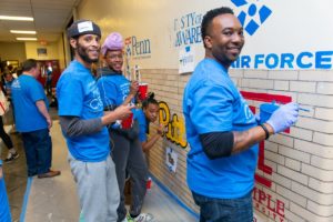 Three volunteers pause from painting college logos on an interior school wall to smile for the camera